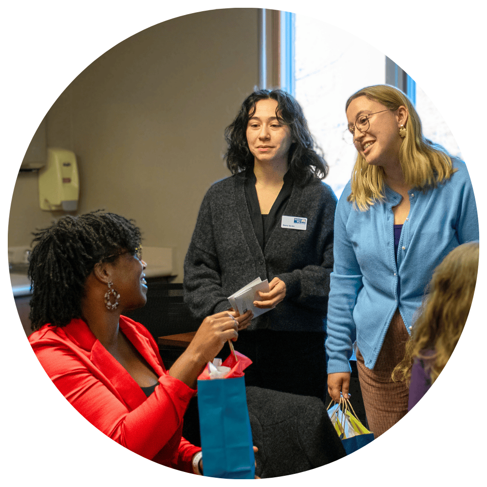 Photo of two smiling women handing a bag to another smiling woman