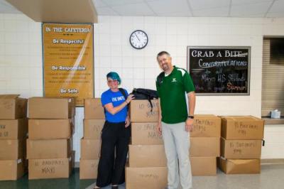 United Way Staff Member and School Employee stand side by side in front of boxes full of backpacks and school supplies