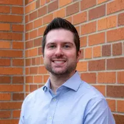 Photo of a smiling white man posing in front of a brick wall